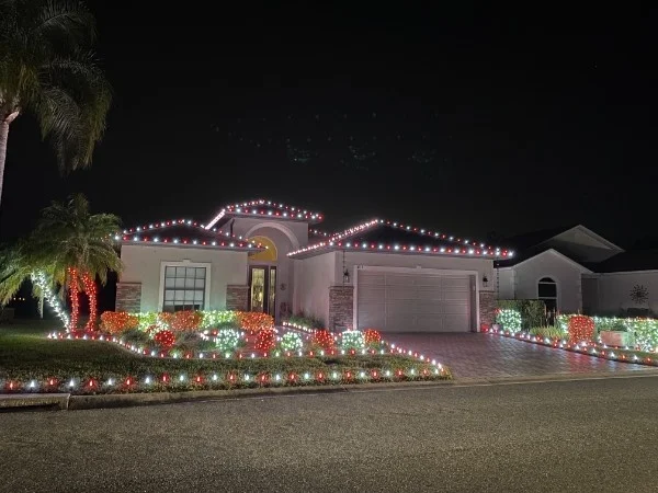 Single-story home with red and white roofline lights and red, green, and white lit shrubs along the front beds