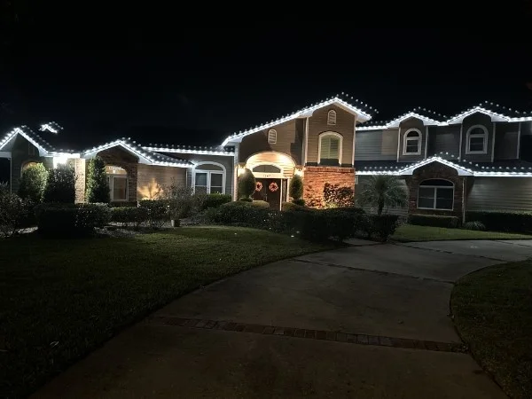Brick and siding home at night with crisp white lights outlining the gables and rooflines